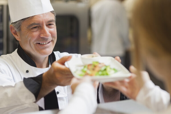 Koch reicht einer Person einen Teller mit Essen