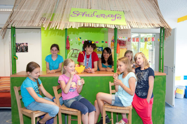 Kinder sitzen und stehen um eine Theke mit Aufschrift "Schülercafé"