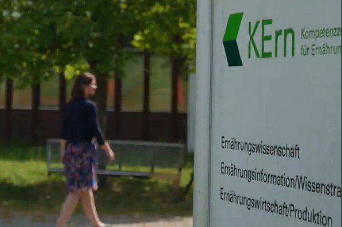 Frau im Hintergrund geht an Schild KErn - Kompetenzzentrum für Ernährung vorbei