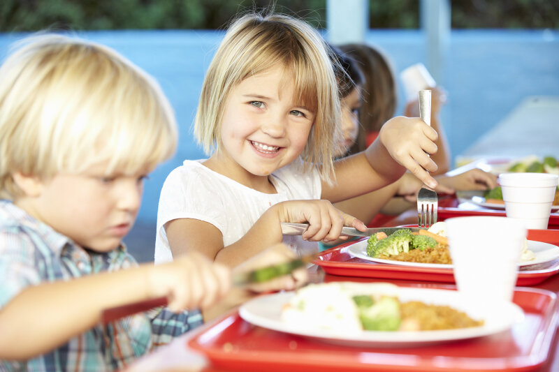 Kinder sitzen vor Tisch mit Tellern mit Essen und Getränken