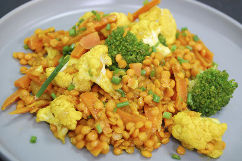 Linsencurry mit Broccoli und Blumenkohl auf weißem Teller angerichtet