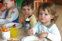 Drei kleine Kinder sitzen am Tisch und essen