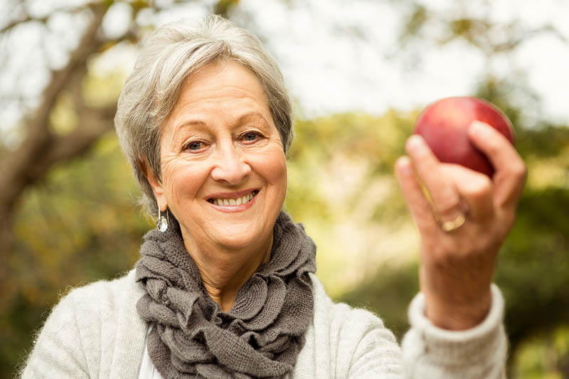 Ältere Dame hält einen Apfel in der Hand – Netzwerk Generation 55plus