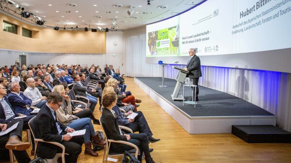 Ein Mann steht auf einem Podium und hält vor Publikum eine Rede