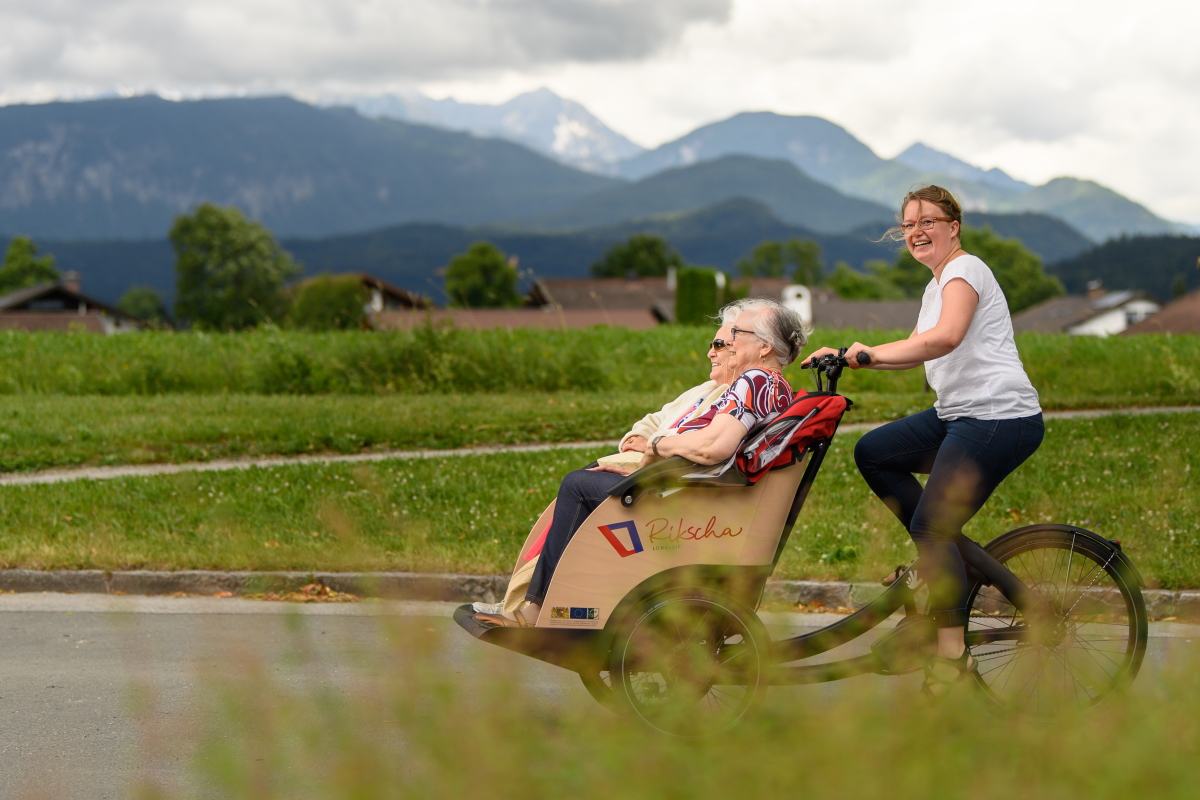 Eine junge Frau fährt zwei Seniorinnen in einer Rikscha