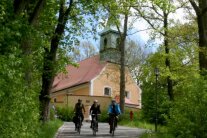 Drei Radfahrer fahren von einer Kapelle weg