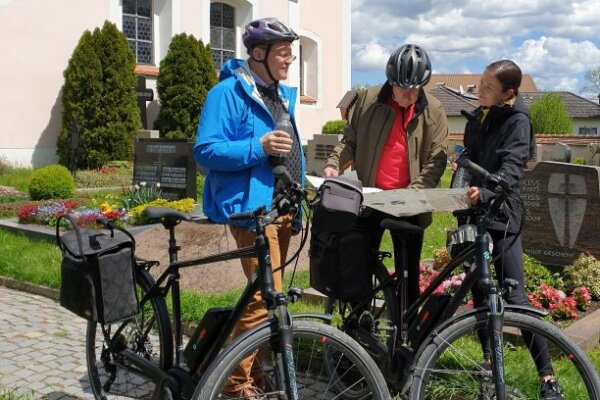 Drei Radfahrer stehen vor einer Kirche