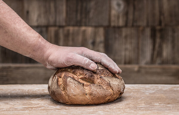 Hand eines Bäckers liegt auf einem Laib Brot