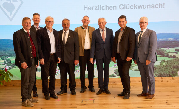 Acht festlich gekleidete Männer stehen in einer Reihe auf der Bühne