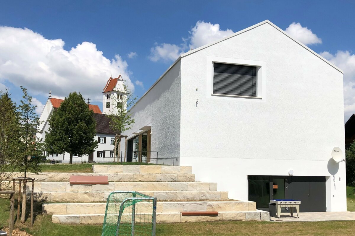 Das Dorfgemeinschaftshaus sieht man nun von hinten mit einer großstufigen Steintreppe zum Parkplatz.