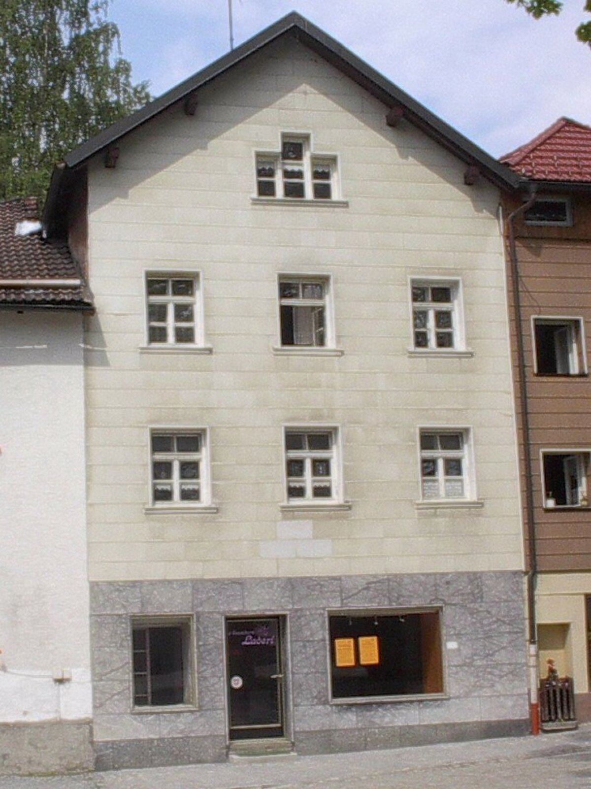 Die Fassade des dreistöckigen Wohnhauses in seiner alten grauen Erscheinung von der Sanierung ist zu erkennen.