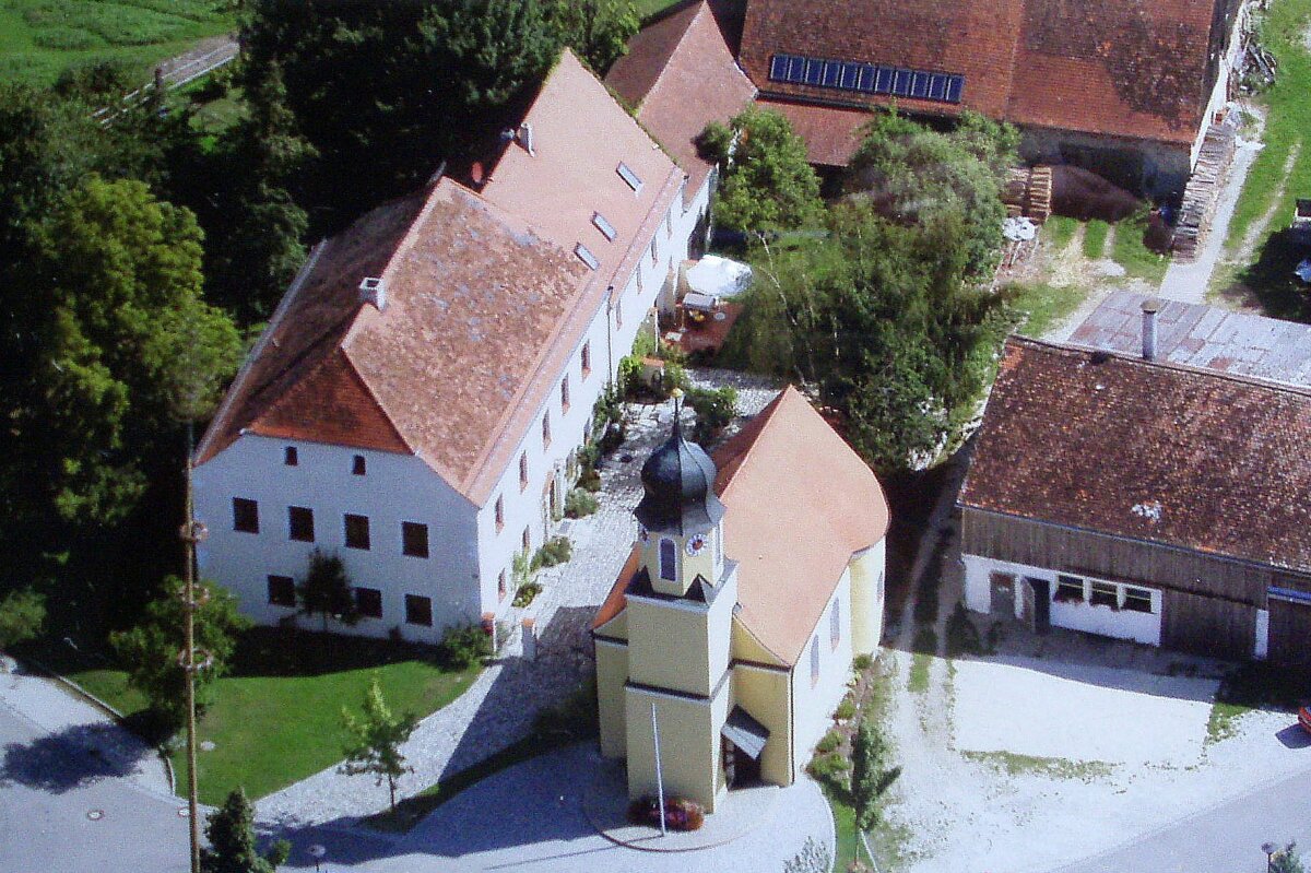 Gesamtansicht des Schlossensembles von oben: von links saniertes Wohnhaus, daneben Kapelle, dahinter markanter Baum, großer Stadel.