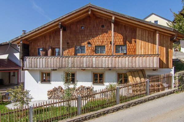 Ein Haus mit Holzbalkon und Holzfassade, davor steht ein Holzzaun.