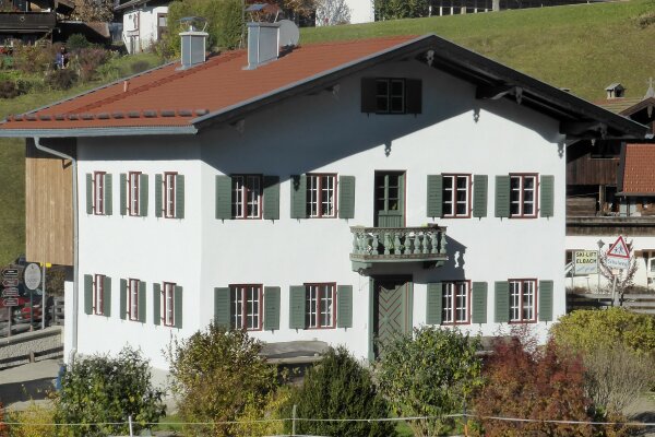 Zweigeschossiger Einfirsthof mit weißer Fassade sowie roten Fensterrahmen, grünen Fensterläden und Türen. Sechsfelderige Sprossenfenster 