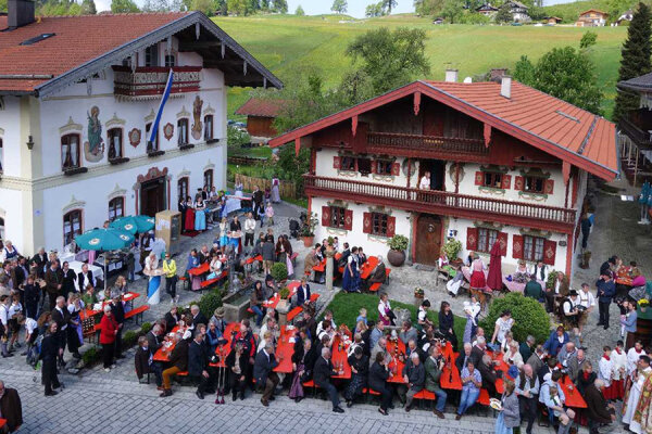 Ein Dorfplatz bestückt mit Bierbänken und Tischen auf denen viele Menschen sitzen.