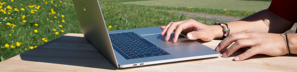 Eine Frau arbeitet in der Natur auf ihrem Laptop.