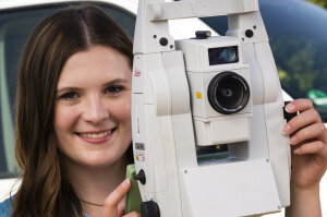 Mädchen steht hinter einem Tachymeter (Vermessungsinstrument)