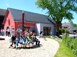 Kinder auf dem Spielplatz, im Hintergrund neu geschaffenes Gemeinschaftshaus