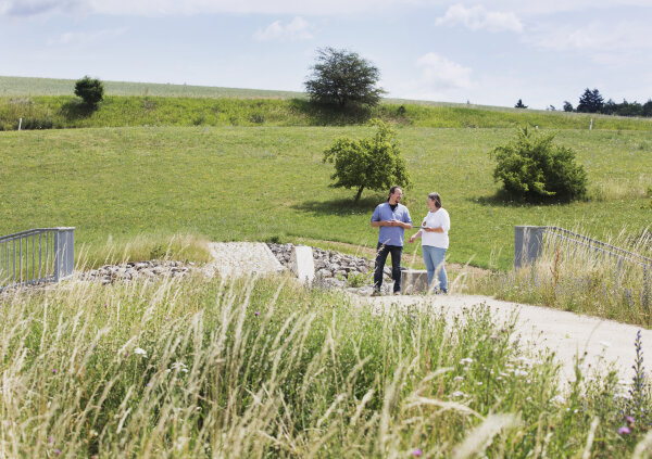 Bild zwei Menschen in einer grünen Landschaft, einer deutet auf etwas in der Ferne.