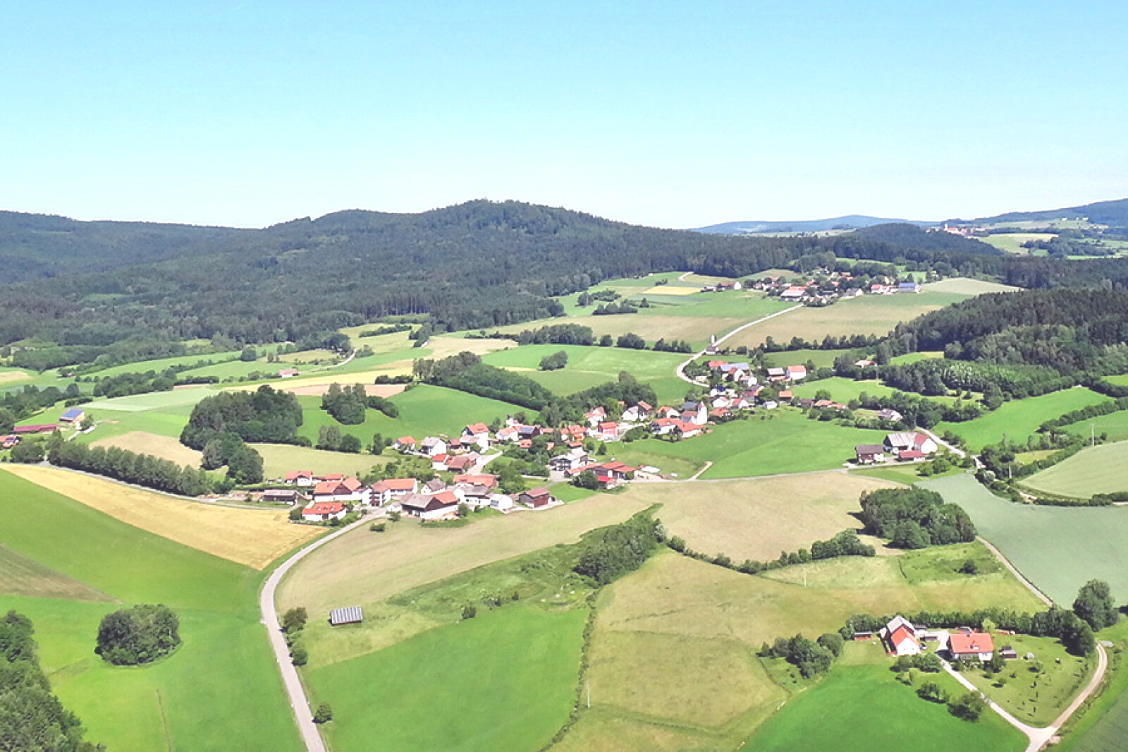 Ein kleines idyllisches Dorf zwischen kleinem Wald, Feldern, Hecken und Wiesen