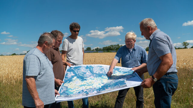 Bürger stehen auf einem Feld und schauen sich gemeinsam einen Plan an.