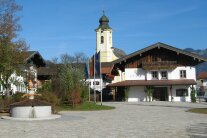 Der neugestaltete Schlechinger Dorfplatz mit Brunnen und Rathaus, der Kirchturm erhebt sich dahinter.