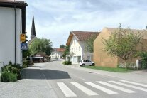 Straße durch ein Dorf mit Zebrastreifen. Ein beiges Modellhaus ergänzt die dörfliche Häuserzeile.