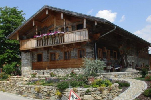 Ein niederbayerisches Waldlerhaus mit Balkon steht auf einem mit Steinen befestigten Hügel.