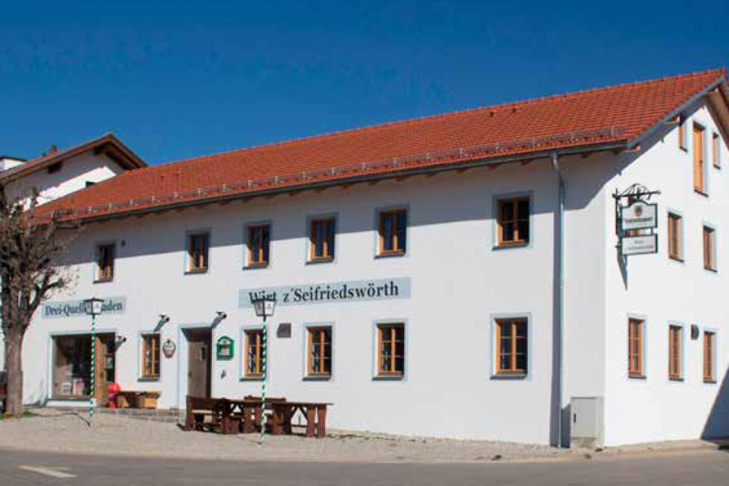 Ein Gasthaus mit weißer Fassade und Holzfenster wurde saniert und ein Dorfladen integriert.