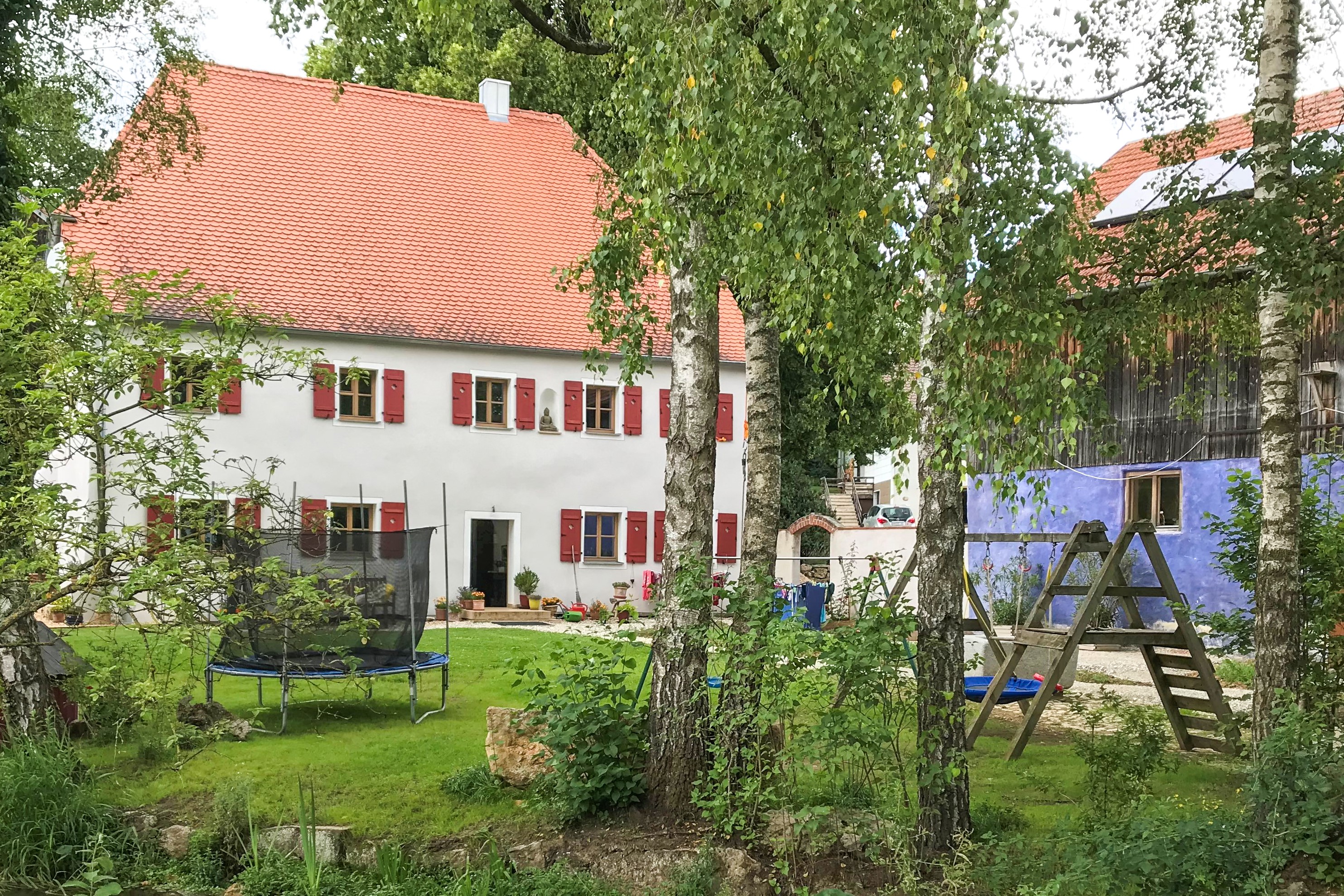 Ein prächtiges Mühlengebäude ist mit vielen Bäumen und einem Spielplatz umgeben