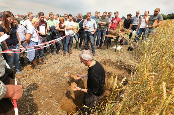 Wissenschaftler in einem Feld erklärt den Teilnehmerinnen und Teilnehmern Fachliches zur Bodenerosion