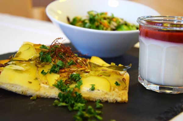 Stück Flammkuchen, Salat in einer Schale und Glas mit Joghurt und Fruchtsauce