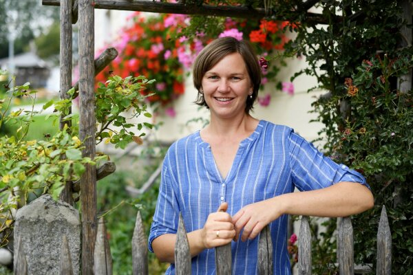 Frau steht am Gartenzaun ihres Hausgartens