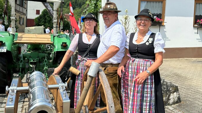 Zwei Frauen und ein Mann an einer großen Kanone, die an einem Traktor hängt.