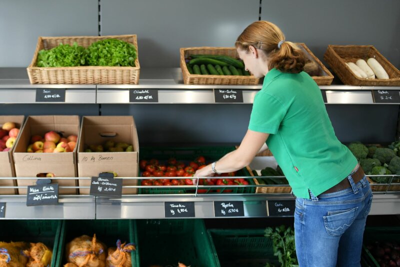 Frau bestückt Obst- und Gemüseregal in einem Hofladen