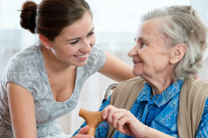 Pflegerin hilft älterer Frau mit Gehstock