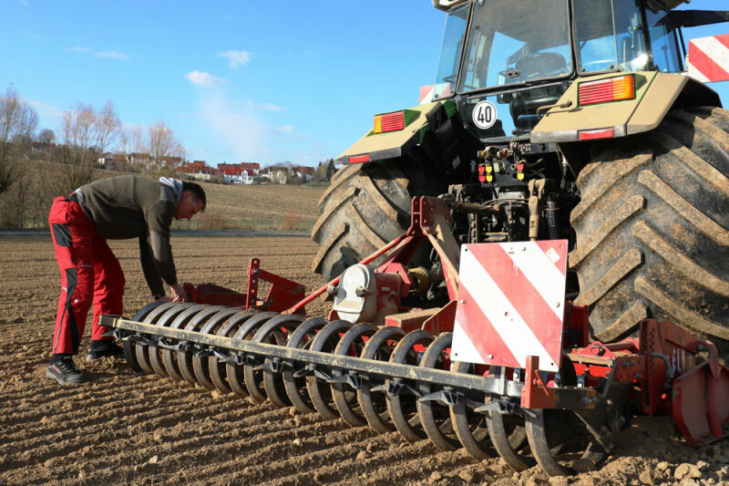 Mann beugt sich über eine Kreiselegge an einem Traktor auf dem Feld