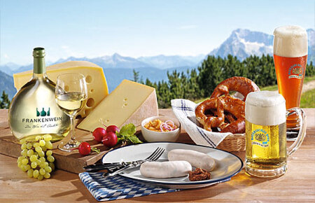 Tisch mit Brotzeit, Weißwürste, Käse, Brezen, Wein und Bier.
