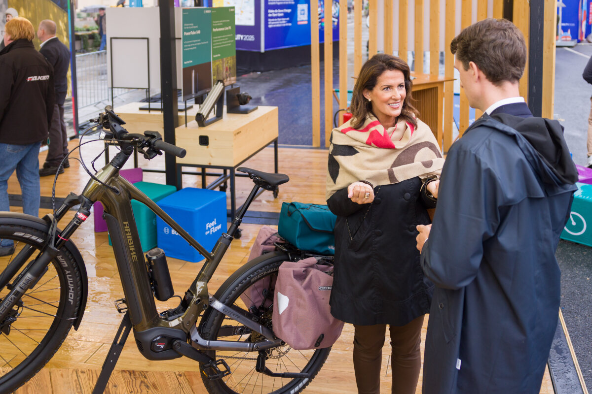 Ministerin Kaniber zusammen im Gespräch mit einem Mann am Stand eines E-Bike Herstellers, sie stehen neben einem E-Bike.