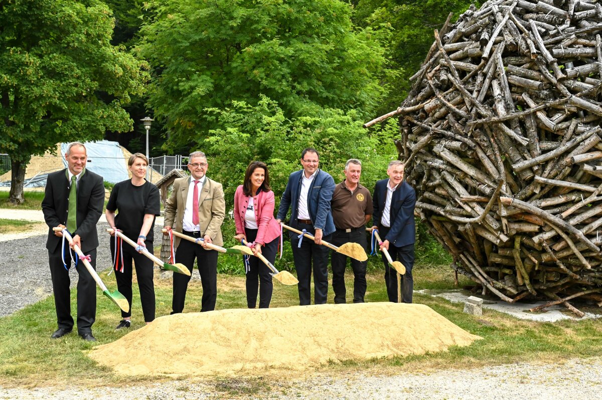 Das Bild zeigt Staatsministerin Kaniber gemeinsam mit anderen Teilnehmern beim symbolischen Spatenstich mit Spaten in der Hand vor einem Sandhaufen.