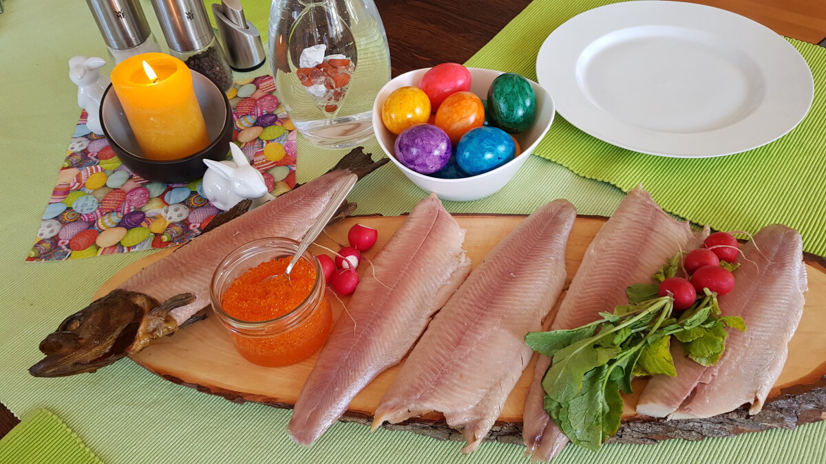 Geräucherte Forellenfilets auf Holzbrett. Im Hintergrund eine Dekoration mit gefärbten Osterfeiern