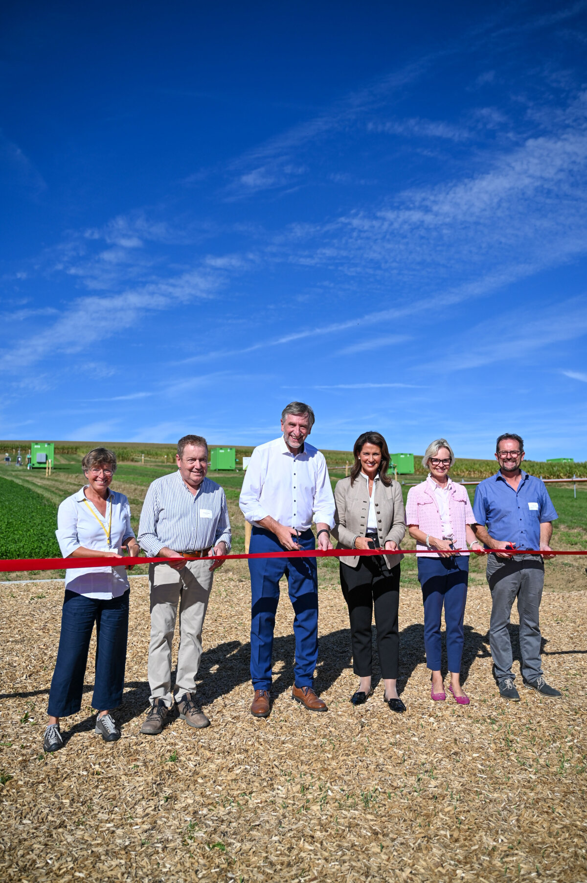 Die Ministerin und andere Beteiligte stehen auf einem Feld und schneiden symbolisch ein rotes Band zur Eröffnung der Anlage durch.