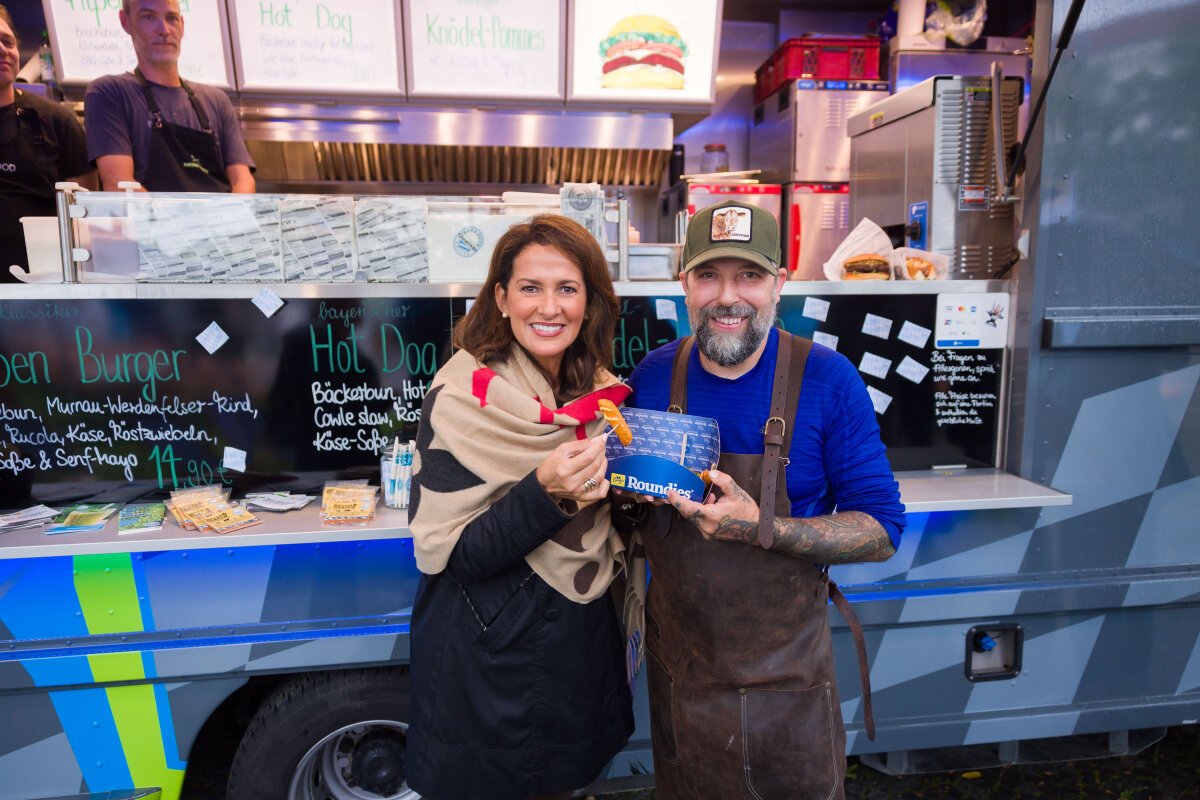 Die Ministerin steht zusammen mit einem Mitarbeiter vor einem Foodtruck und präsentiert Essen.