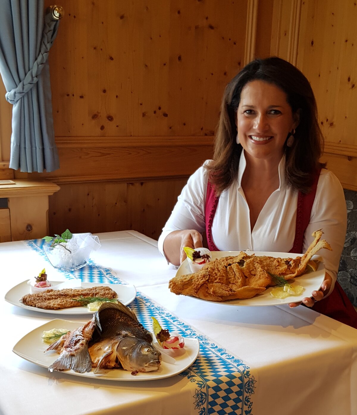 Ministerin Michaela Kaniber sitzt an einem Tisch und hält eine Platte in der Hand mit verschiedenen Karpfenprodukten