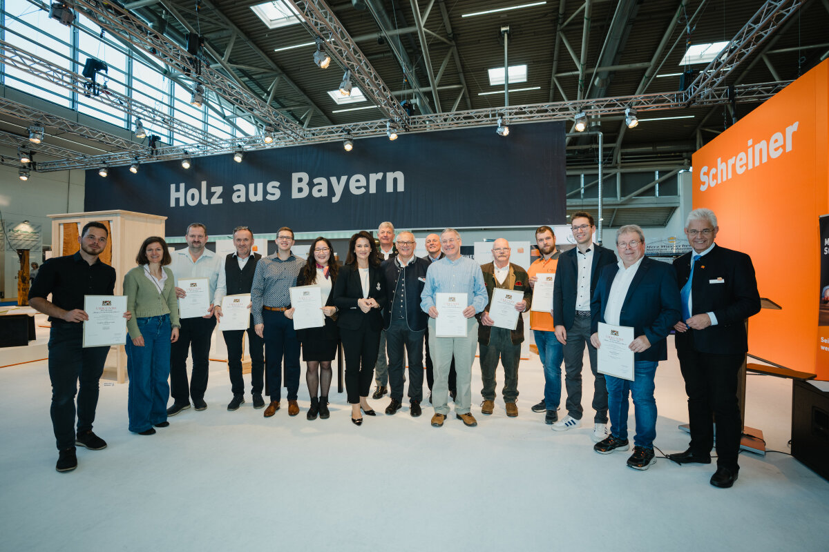 Ministerin Kaniber mit den Preisträgerinnen und Preisträgern in einer Messehalle. Einige halten Urkunden vor sich.