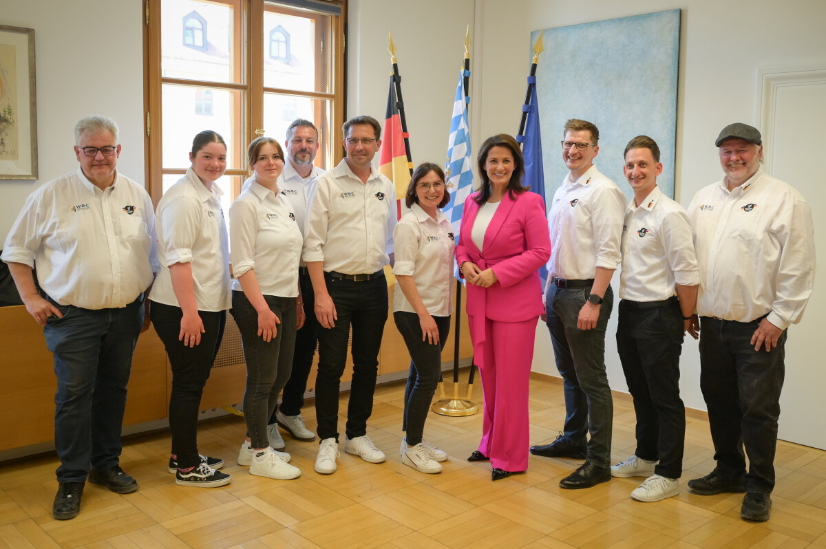 Das Bild zeigt die Staatsministerin zusammen mit Teamkollegen des Butcher Wolfpack in einem Raum im Ministerium.