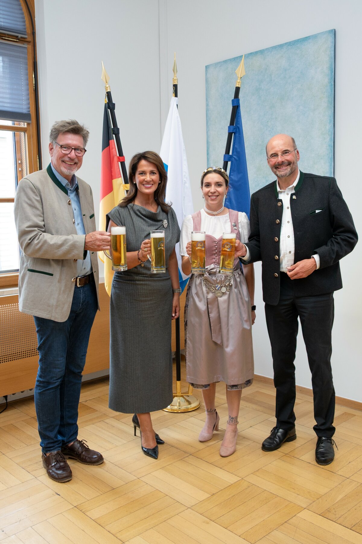 Ministerin Kaniber steht zusammen mit den beiden Funktionären des Bayerischen Brauerbundes sowie der Bierkönigin in ihrem Amtszimmer vor Fahnen. Sie halten alle Krüge mit Bier in den Händen.