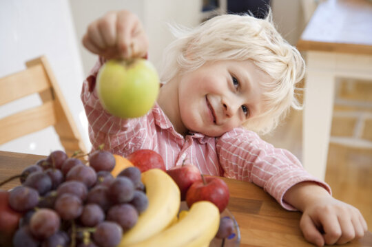 Blonder Junge hinter Obstschale mit Apfel in der Hand