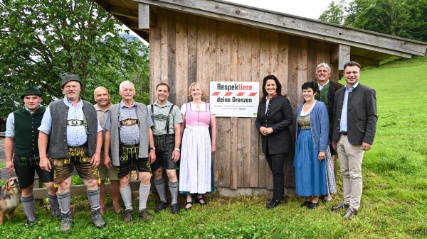 Ministerin Michaela Kaniber mit örtlichen Vertretern und Landwirten vor einem Stadel mit dem Schild der Initiative "Respektiere deine Grenzen"