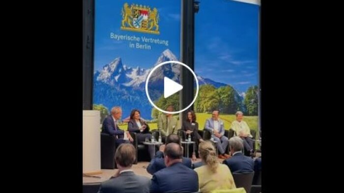 Sechs Personen sitzen auf einer Bühne und diskutieren. 